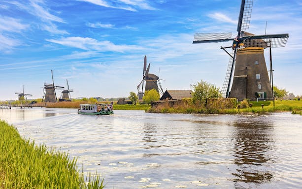 Windmills along a canal in the Dutch countryside with a tour boat cruising.