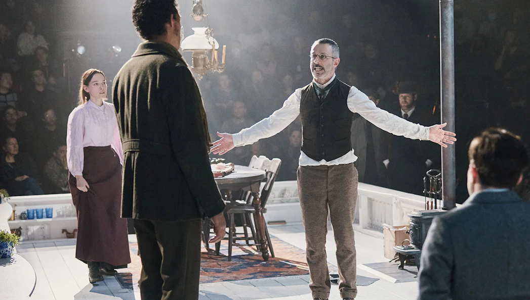 Theater performance of "An Enemy of the People" with actors in period costumes on stage.