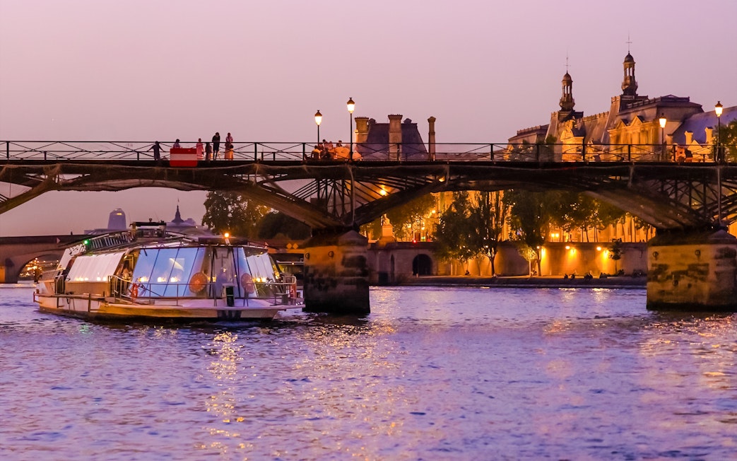 Bateaux Parisiens boat cruising under a lit bridge on the Seine River in Paris, France.