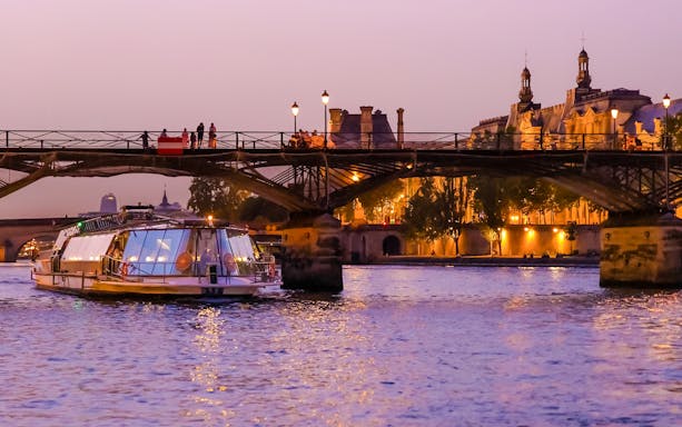 Bateaux Parisiens boat cruising under a lit bridge on the Seine River in Paris, France.