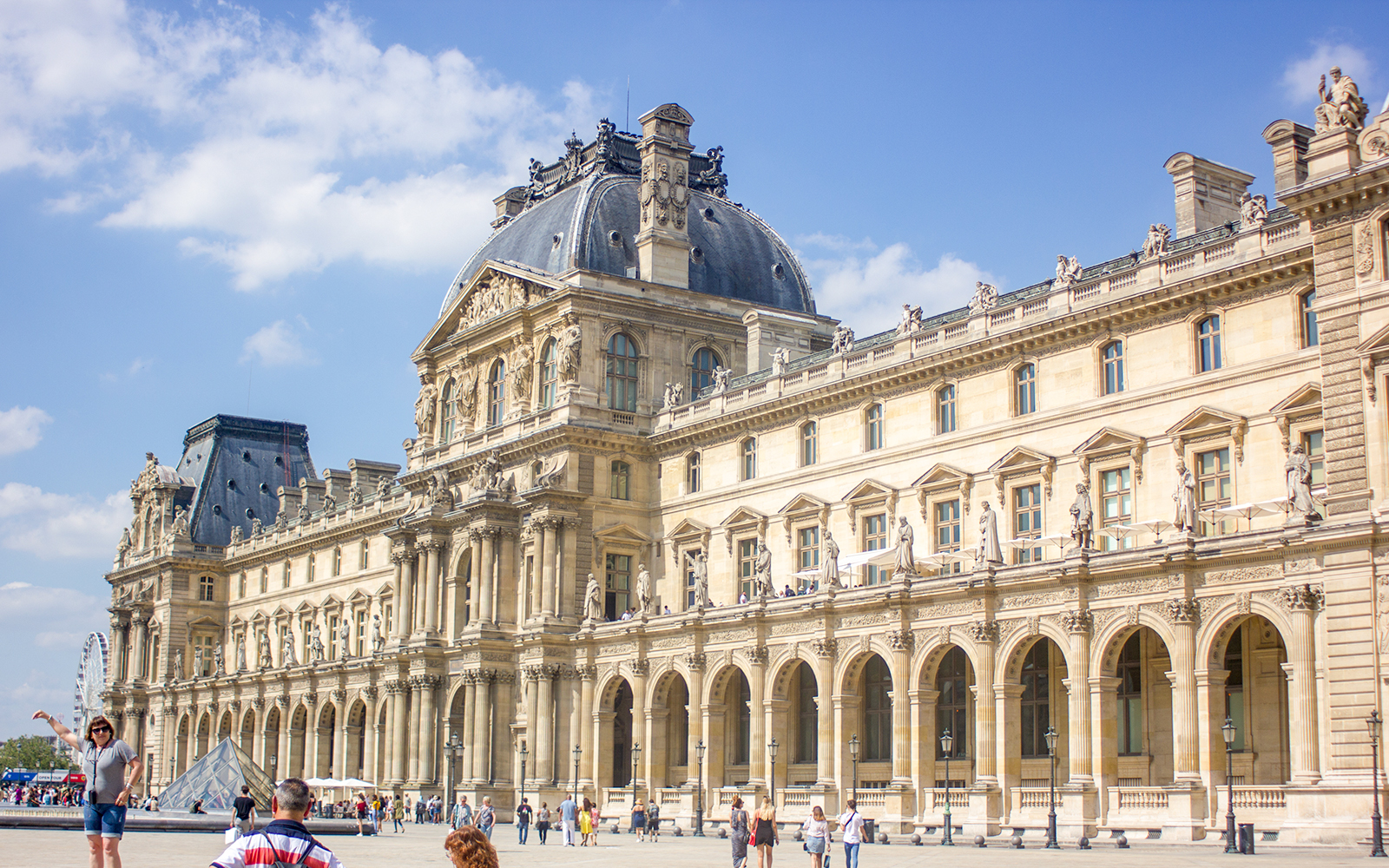 Visitantes explorando el emblemático Museo del Louvre de París, con la famosa entrada en forma de pirámide de cristal.