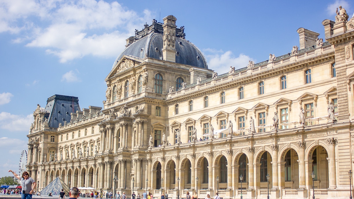 Tourists exploring the iconic Louvre Museum in Paris, featuring the famous glass pyramid entrance