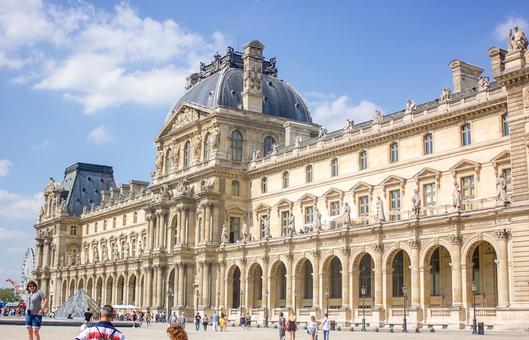 Tourists exploring the iconic Louvre Museum in Paris, featuring the famous glass pyramid entrance