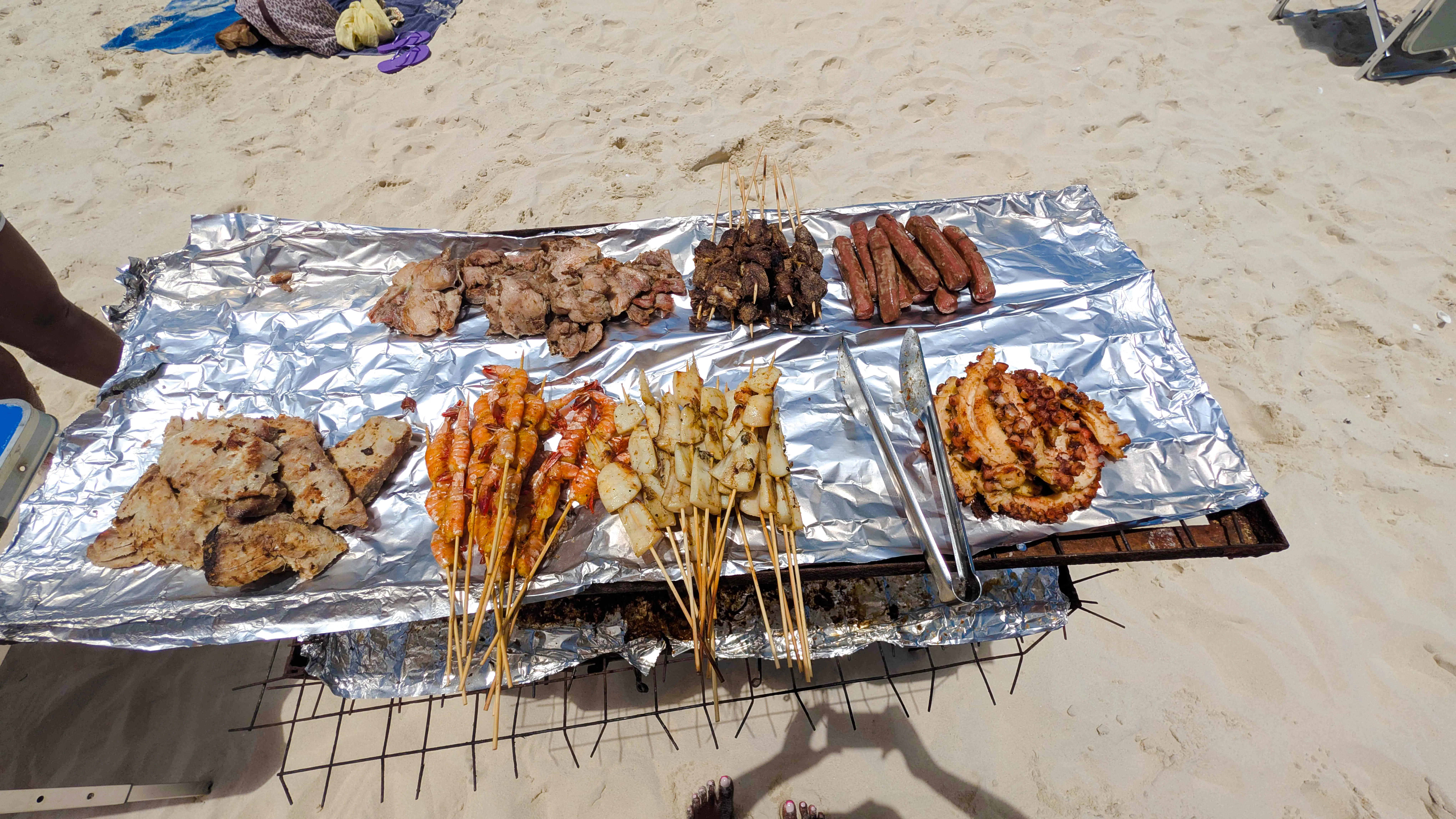 Grilled seafood and meats on foil at a beach BBQ in Zanzibar.