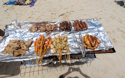 Grilled seafood and meats on foil at a beach BBQ in Zanzibar.