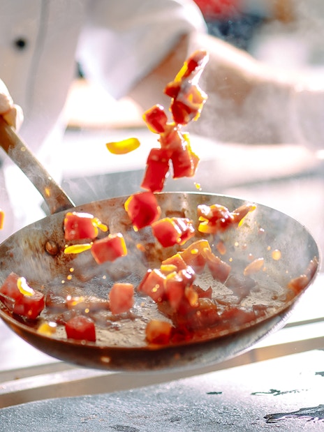 Chef stir frying colorful vegetables in a pan.