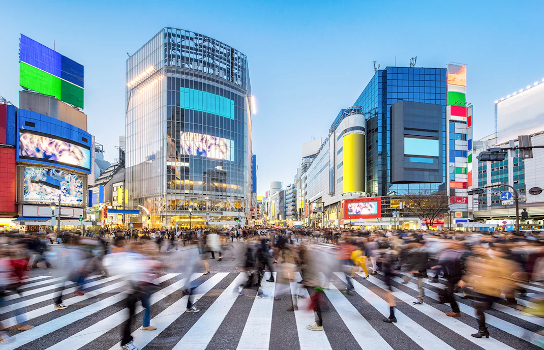 Crowds crossing Shibuya Crossing in Tokyo, Japan with colorful buildings in the background.