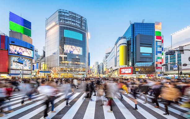 Crowds crossing Shibuya Crossing in Tokyo, Japan with colorful buildings in the background.