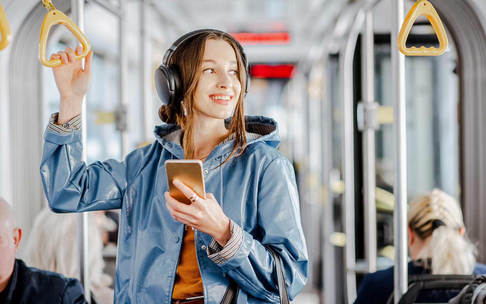 A young girl with a blue jacket standing in a bus whilst enjoying music.