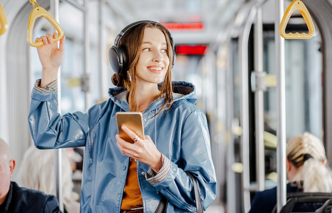 Person listening to music on headphones while holding a phone on a city tram.