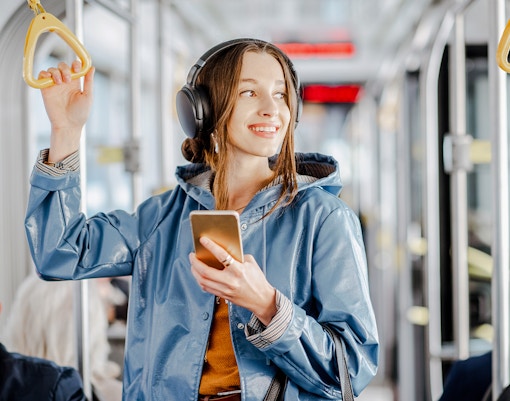 A young girl with a blue jacket standing in a bus whilst enjoying music.