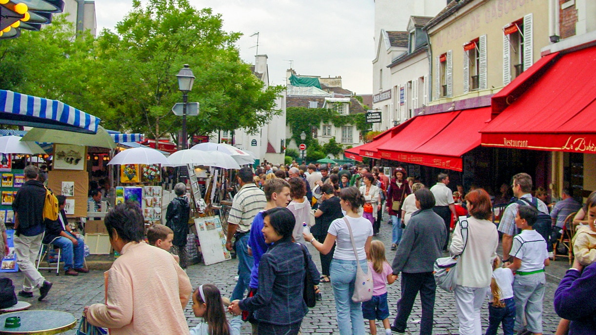 Crowded Montmartre market street with people exploring art stalls and cafes.