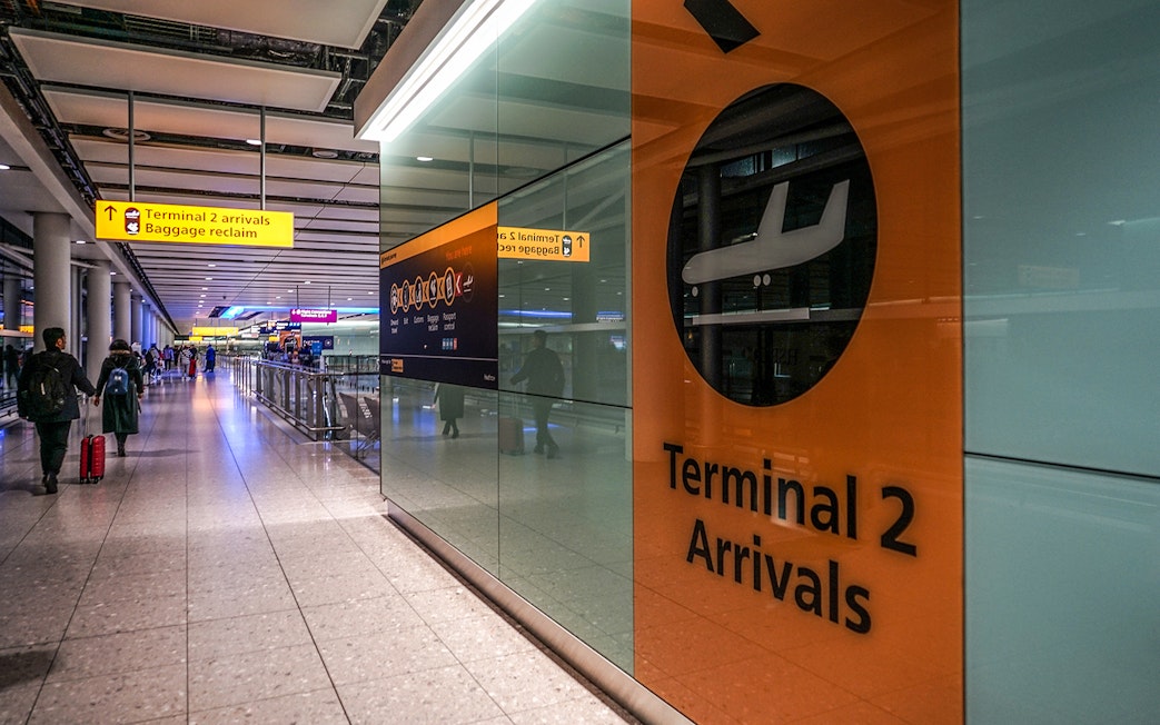 Heathrow Airport Terminal 2 arrivals area with passengers and signage.