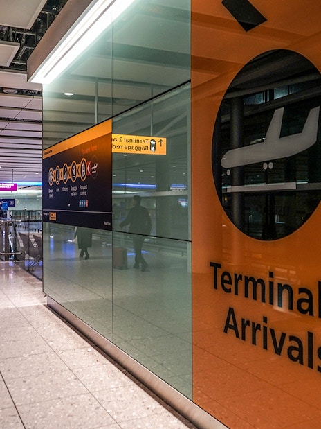Heathrow Airport Terminal 2 arrivals area with passengers and signage.