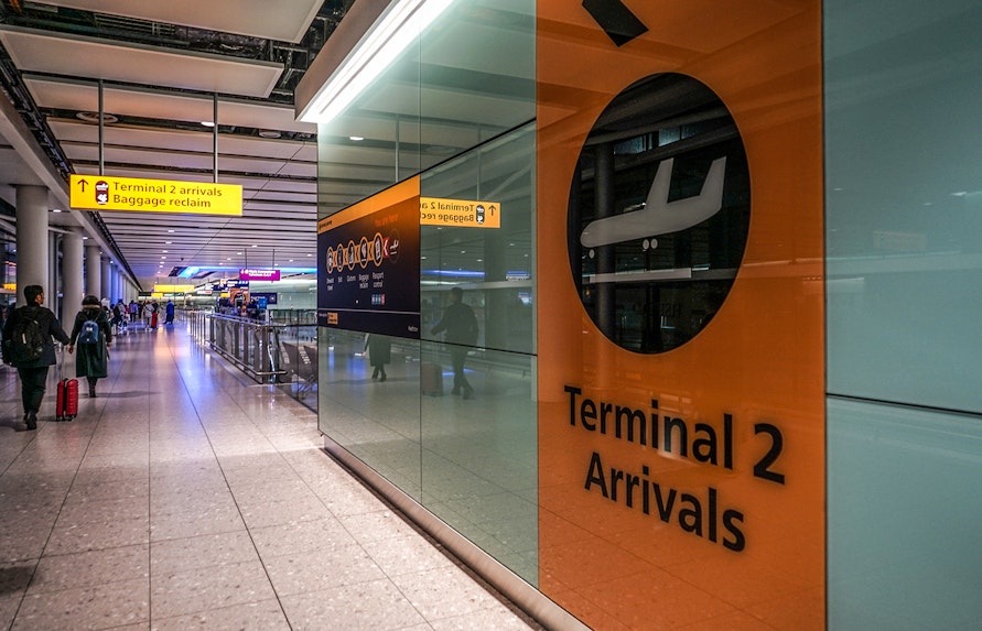 Heathrow Airport Terminal 2 arrivals area with passengers and signage.
