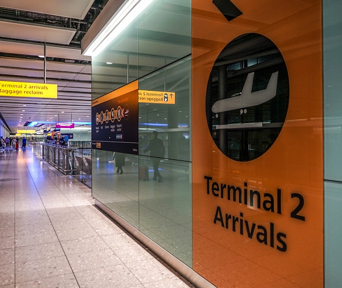 Heathrow Airport Terminal 2 arrivals area with passengers and signage.