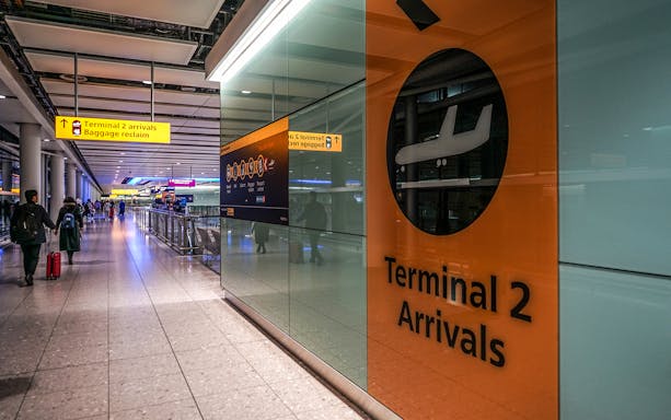 Heathrow Airport Terminal 2 arrivals area with passengers and signage.