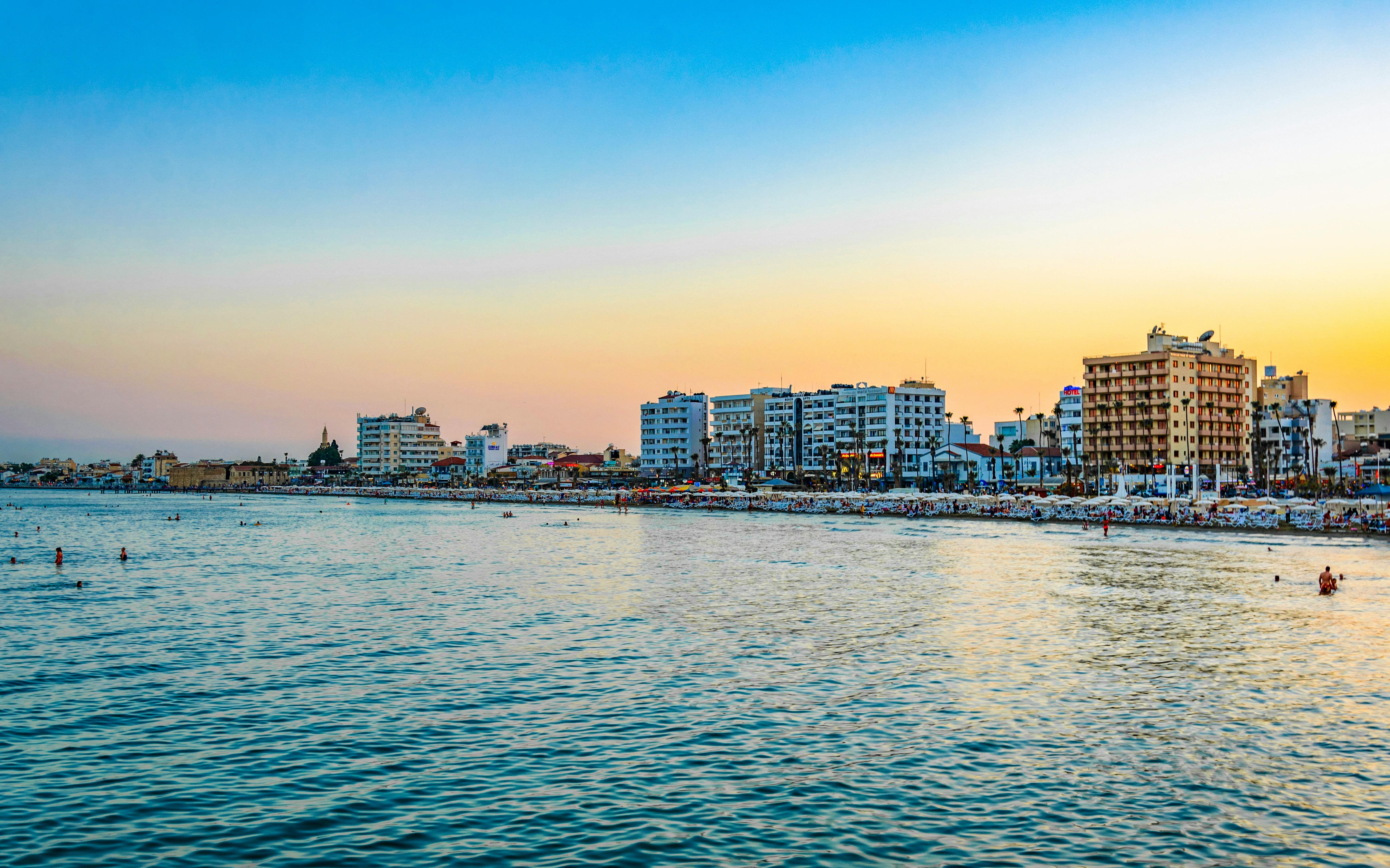 Sunset view of Larnaca coastline with buildings and beachgoers, Cyprus.