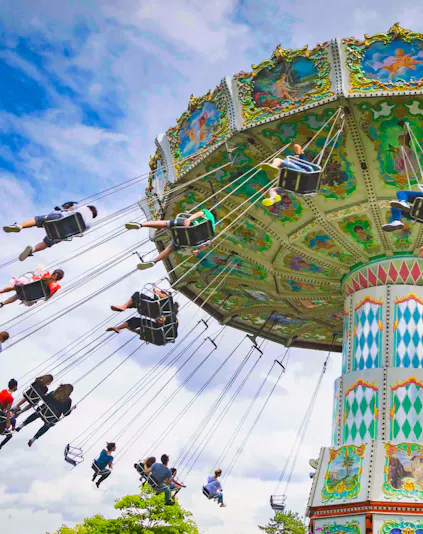Carousel swing ride at Le Jardin d'Acclimatation, Paris, with people enjoying the attraction.