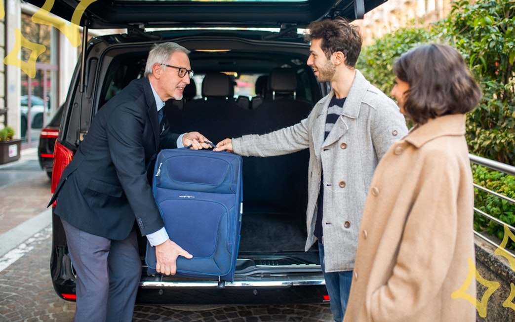 Chauffeur assisting couple with luggage into private airport transfer taxi.