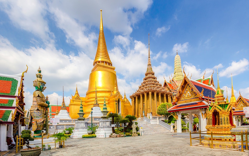 Wat Phra Kaew temple complex with golden stupa and guardian statue, Grand Palace, Bangkok.