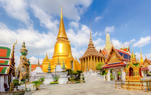 Wat Phra Kaew temple complex with golden stupa and guardian statue, Grand Palace, Bangkok.