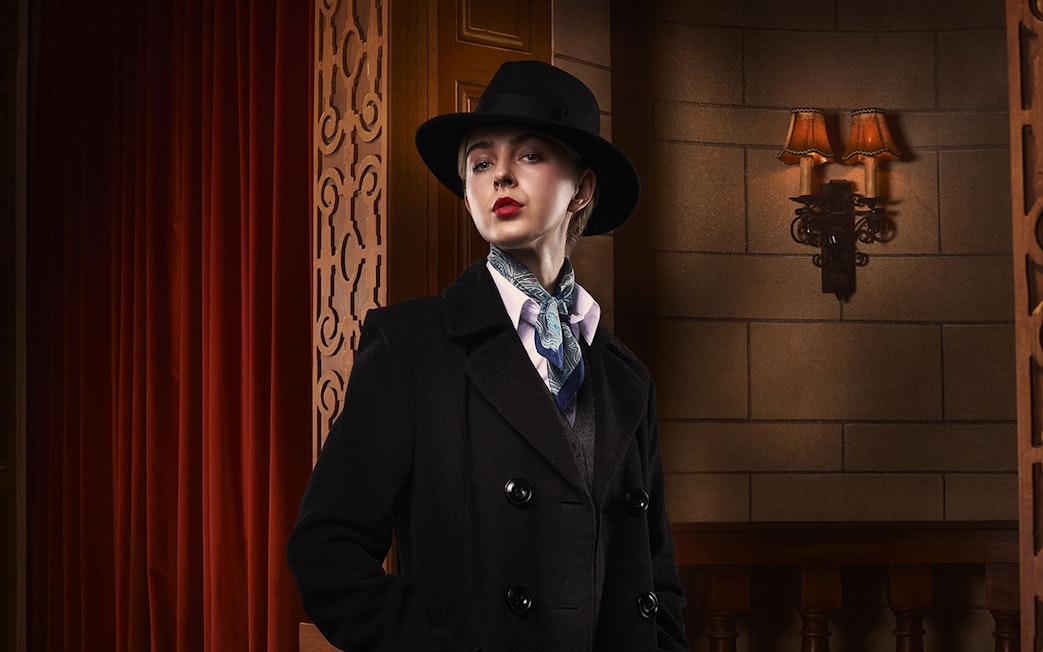 Person in vintage attire with hat and scarf, standing in a theater setting for The Mousetrap.