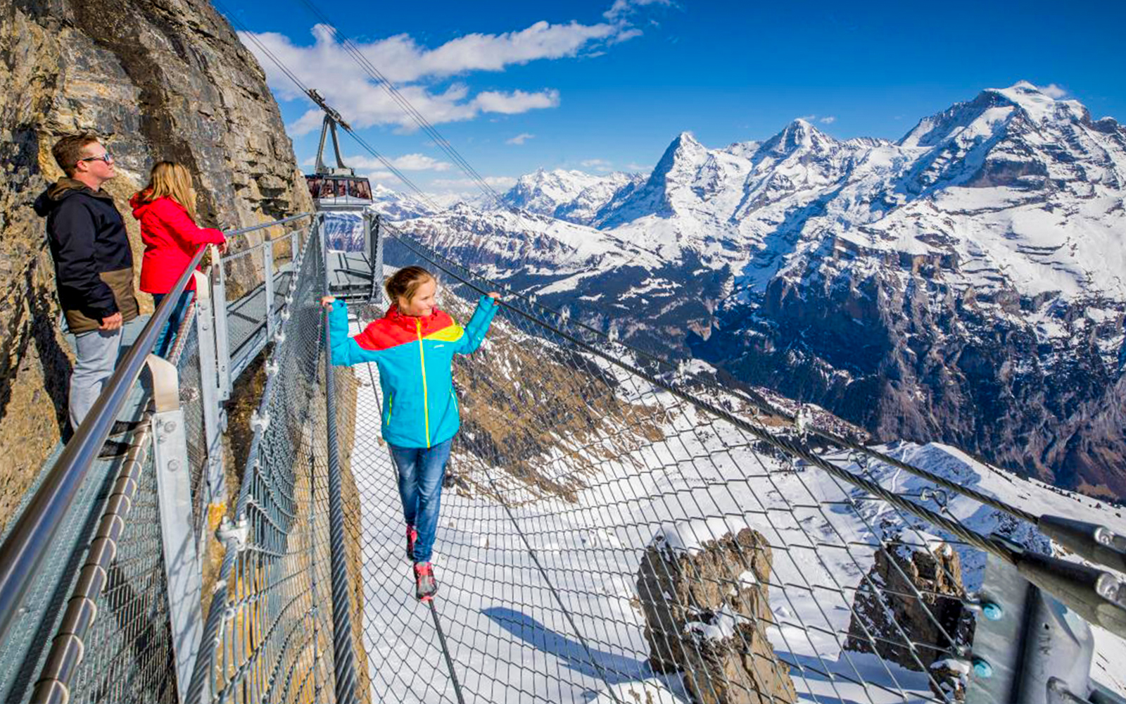 Visitors on a walkway with Schilthorn cable car and snowy Swiss Alps in the background.