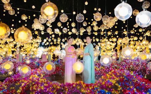 Women in traditional attire at Nasatta Light Festival, surrounded by colorful lights, Bangkok.