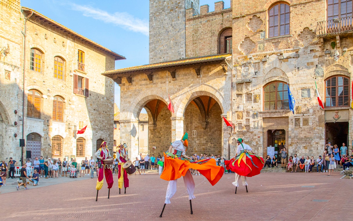Street performers on stilts in a historic square in San Gimignano, Tuscany.
