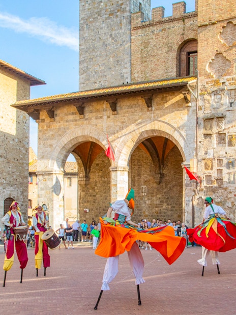 Street performers on stilts in a historic square in San Gimignano, Tuscany.