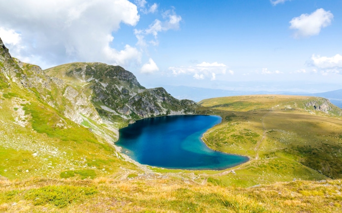 Kidney Lake in Rila Mountain, Bulgaria, surrounded by green hills and rocky terrain.