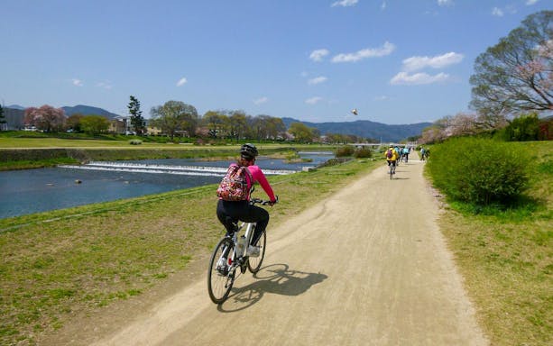 Cyclists on a scenic path along a river in Kyoto during a guided bike tour.