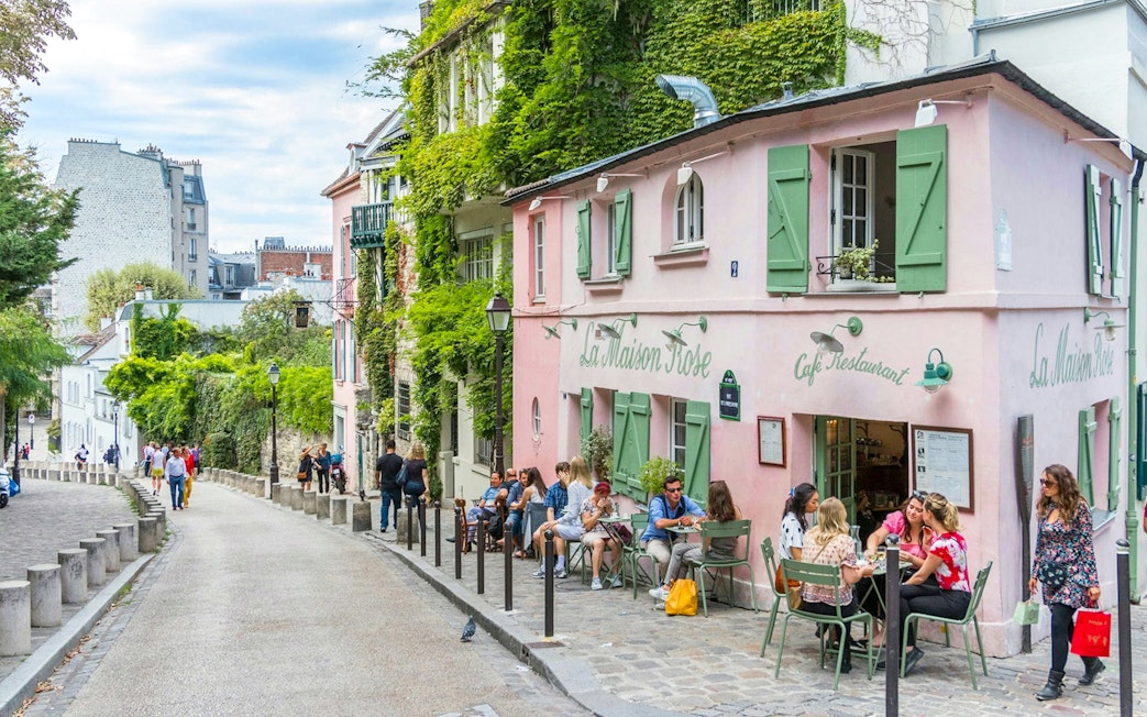 Café La Maison Rose on a cobblestone street in Montmartre, Paris, with people dining outside.