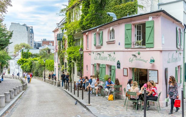 Café La Maison Rose on a cobblestone street in Montmartre, Paris, with people dining outside.