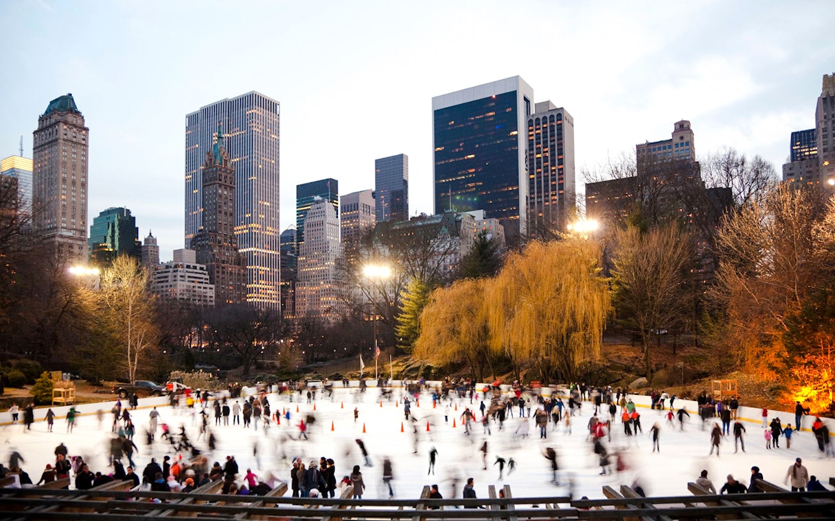 Wollman Rink in Central Park with skaters and New York City skyline.