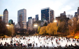Wollman Rink in Central Park with skaters and New York City skyline.
