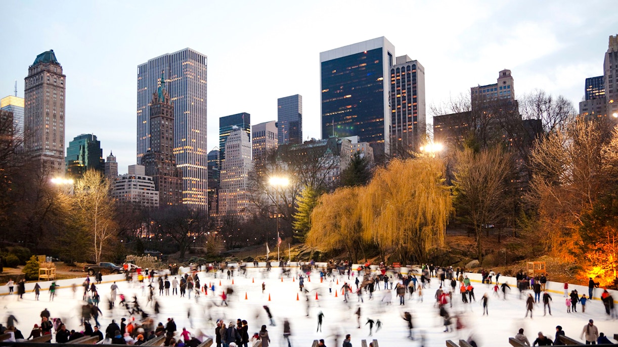 Wollman Rink in Central Park with skaters and New York City skyline.