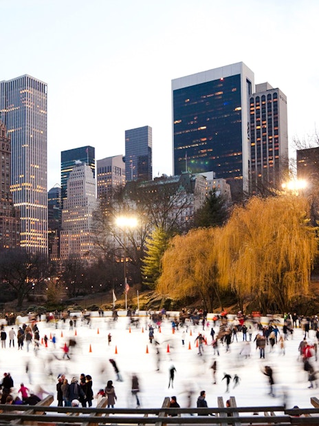 Wollman Rink in Central Park with skaters and New York City skyline.