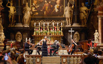 Orchestra performing inside St. Stephen's Cathedral, Vienna, with audience watching.