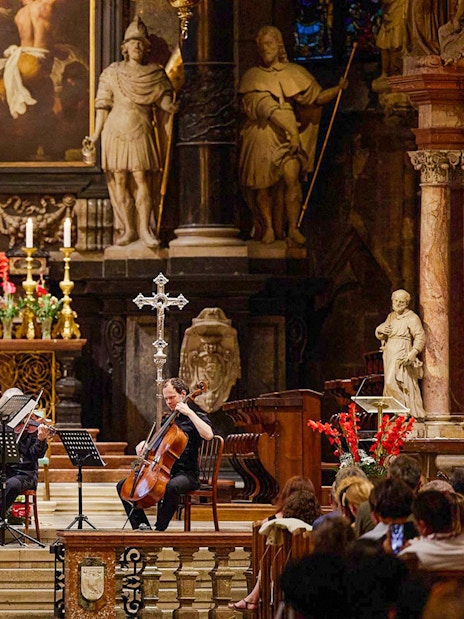 Orchestra performing inside St. Stephen's Cathedral, Vienna, with audience watching.
