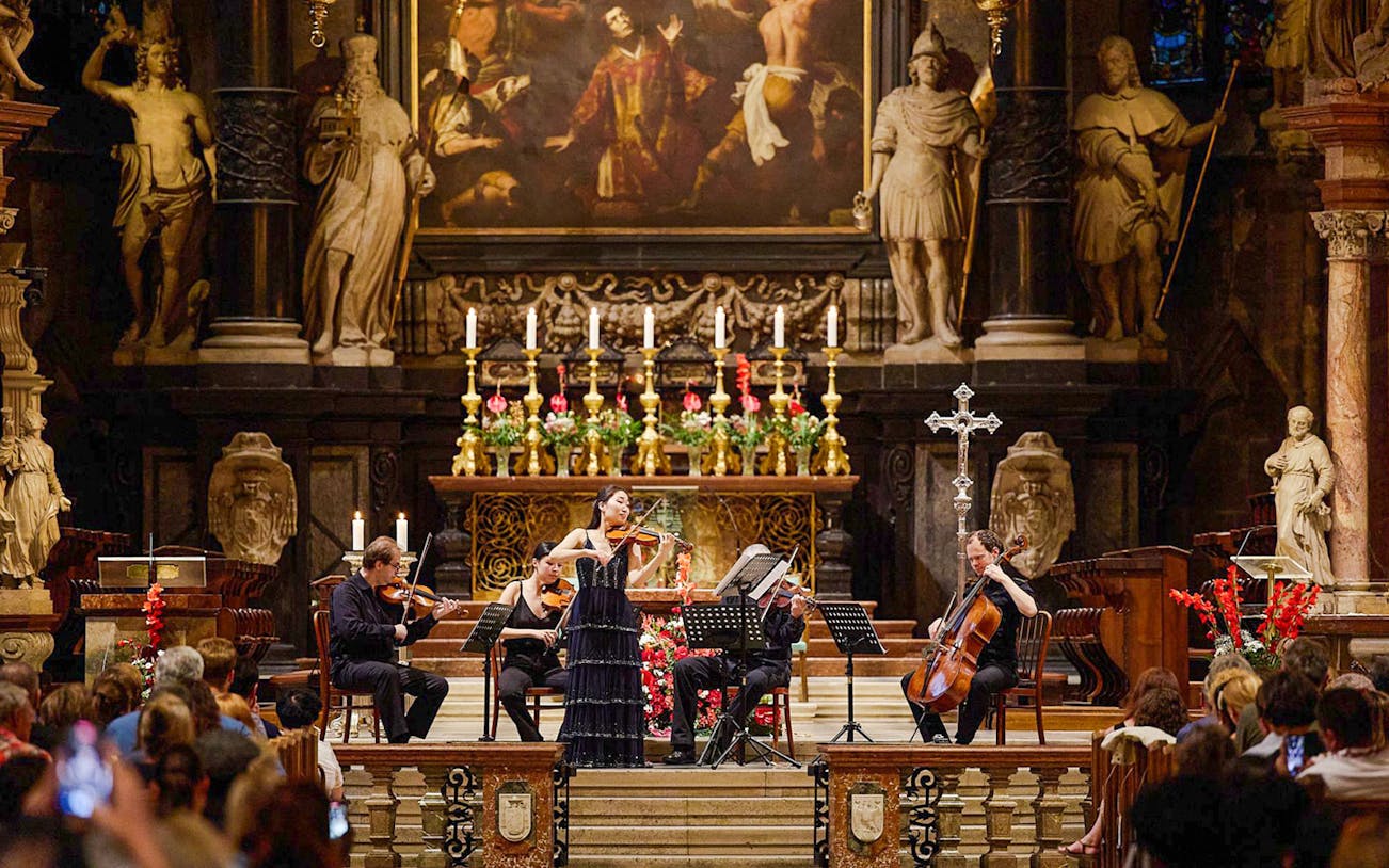 Orchestra performing inside St. Stephen's Cathedral, Vienna, with audience watching.