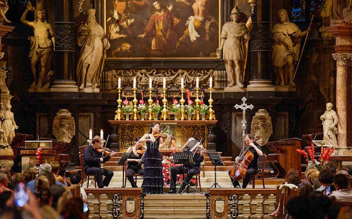 Orchestra performing inside St. Stephen's Cathedral, Vienna, with audience watching.
