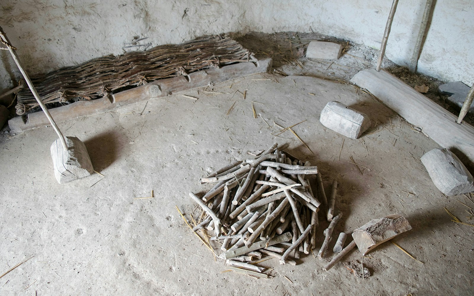 Neolithic house interior at Stonehenge with wooden bed and firewood pile.