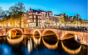 Amsterdam canal with illuminated bridge and historic buildings at dusk.