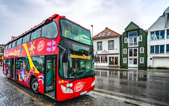 Stavanger hop-on hop-off bus parked near colorful buildings on a rainy street.