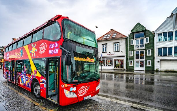Stavanger hop-on hop-off bus parked near colorful buildings on a rainy street.
