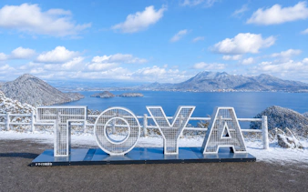 Lake Toya view with snow-covered mountains and large "TOYA" sign, Hokkaido winter tour.
