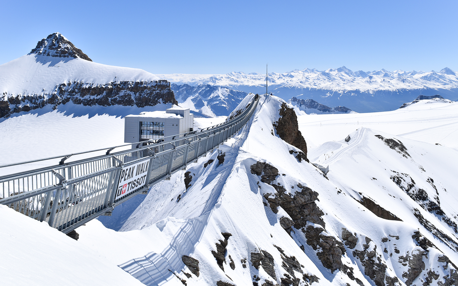 Eine silberne Brücke gührt über eine Schlucht in den verschneiten Schweizer Alpen