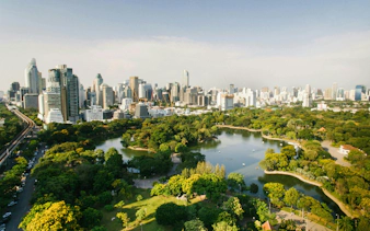 Bangkok skyline with Lumphini Park and lake in the foreground.